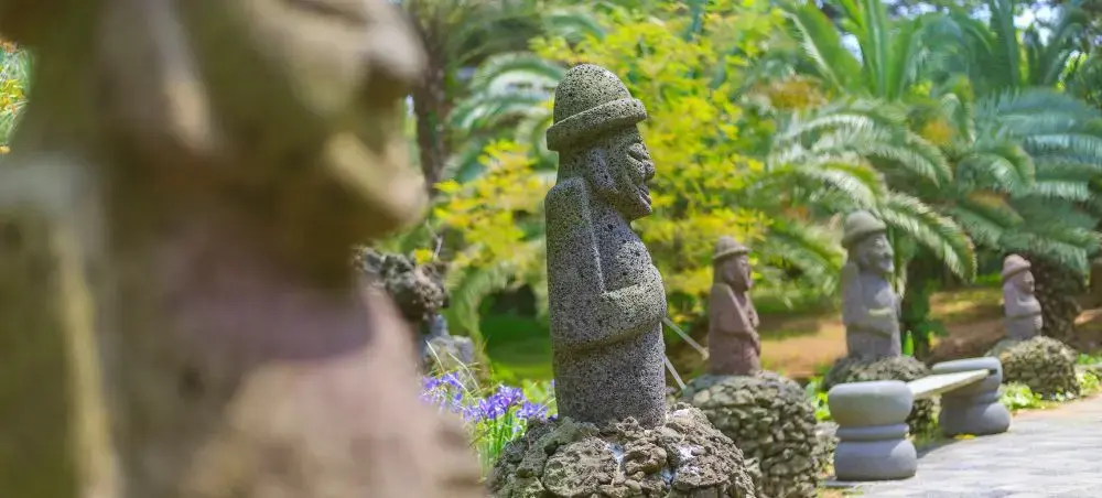 Traditional stone statues called dol hareubang stand among lush tropical gardens in South Korea