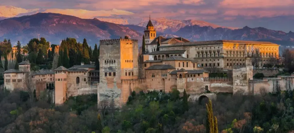 Alhambra palace complex illuminated at sunset with snow-capped Sierra Nevada mountains in Granada, Spain