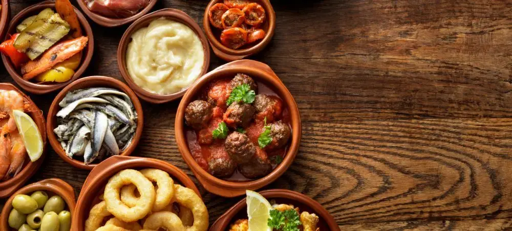 Traditional Spanish tapas spread featuring meatballs, anchovies, olives and dips in terracotta bowls