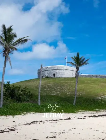 Historic Royal Naval Dockyard fortress overlooking pristine Bermuda beach with swaying palm trees
