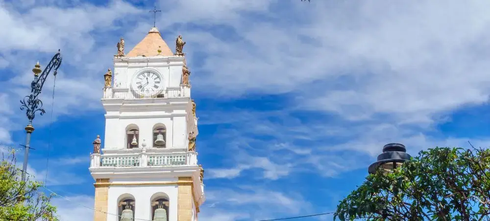 Historic colonial bell tower with ornate white facade and clock under blue sky in Sucre Bolivia
