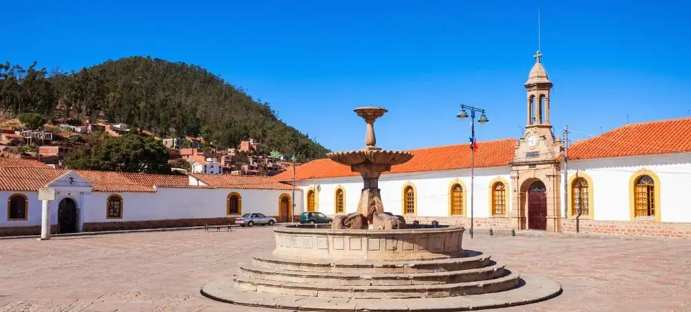 Historic colonial plaza in Sucre with ornate stone fountain and traditional architecture under clear blue sky
