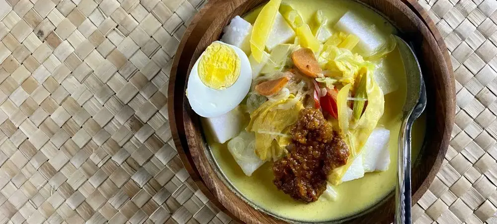 Traditional Indonesian soto ayam soup with hard-boiled egg and vegetables served in wooden bowl on woven mat