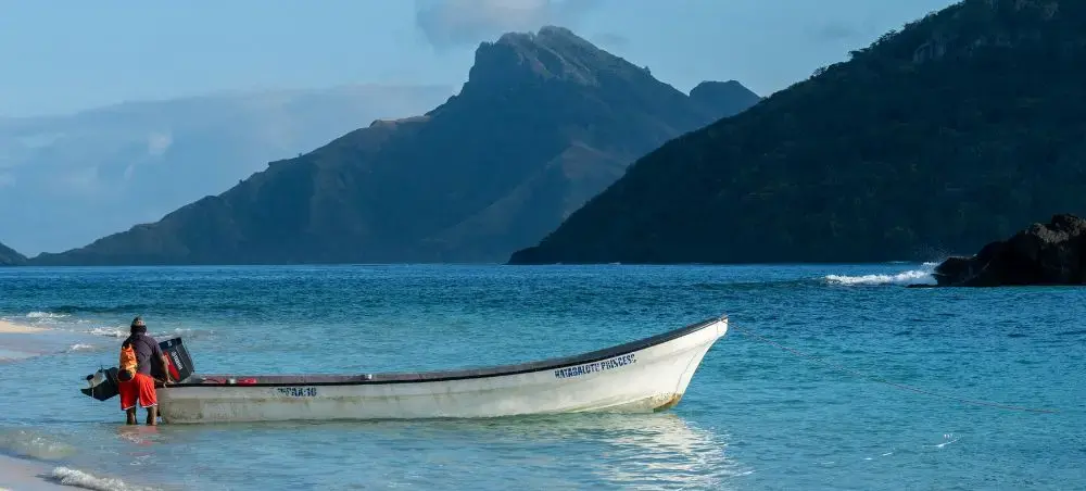 Traditional Fijian fishing boat anchored in pristine turquoise waters near Suva with dramatic mountains