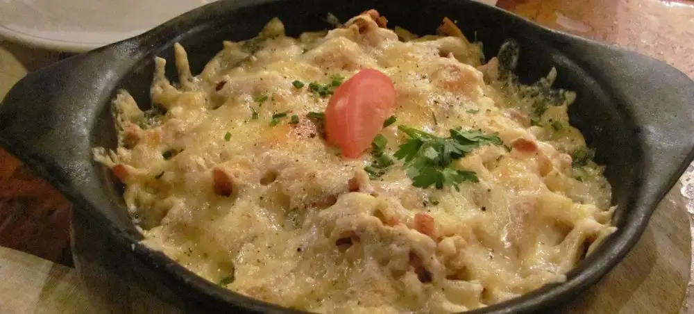 Creamy Swiss cheese fondue with bacon and herbs served in traditional cast iron pan, showcasing Switzerland's culinary heritage
