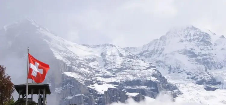 Swiss flag flying proudly against dramatic snow-capped Alpine peaks showcasing Switzerland's majestic mountain landscape