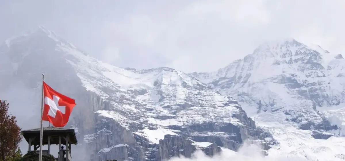 Swiss flag flying proudly against dramatic snow-capped Alpine peaks showcasing Switzerland's majestic mountain landscape