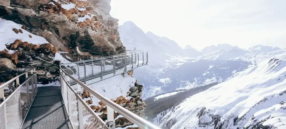 Mountain observation deck with steel walkway overlooking snow-covered Swiss Alpine peaks and valleys