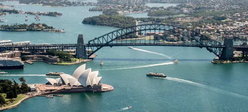 Aerial view of Sydney Harbour featuring the iconic Opera House and Harbour Bridge with luxury boats below