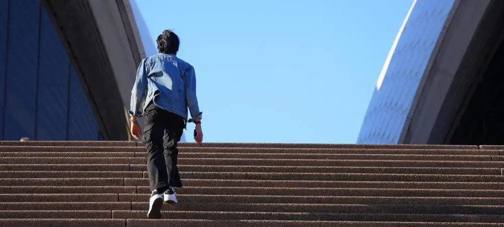 Business traveler ascending modern concrete steps toward Sydney's iconic skyscrapers on clear day