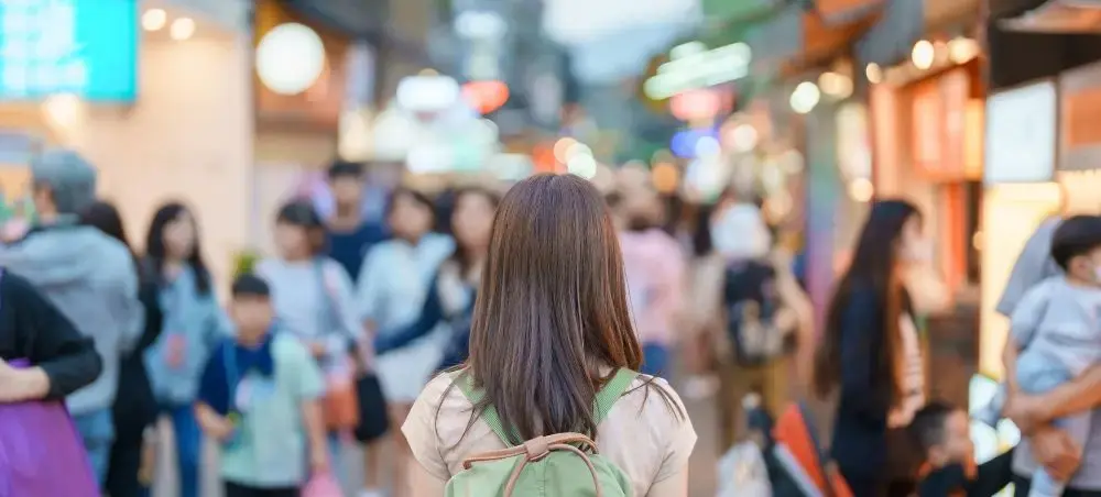 Woman with backpack exploring bustling Taipei street market filled with colorful lights and crowds