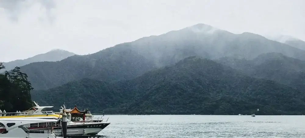 Scenic mountain lake in Taiwan with traditional boats docked at waterfront beneath misty forested peaks