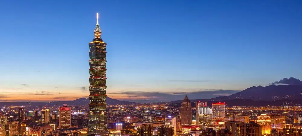 Taipei 101 skyscraper illuminated at dusk with Taiwan's capital city skyline and mountains in background