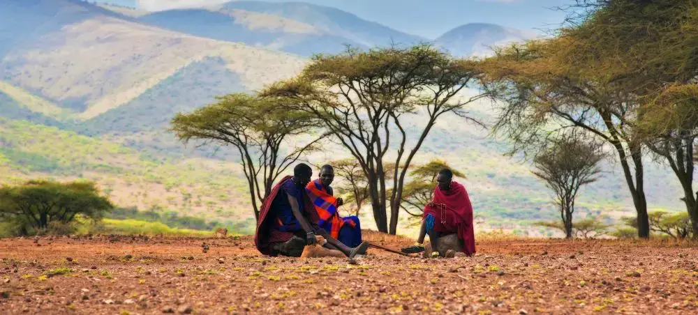Maasai tribesmen in traditional red robes gather under acacia trees in Tanzania's scenic highlands