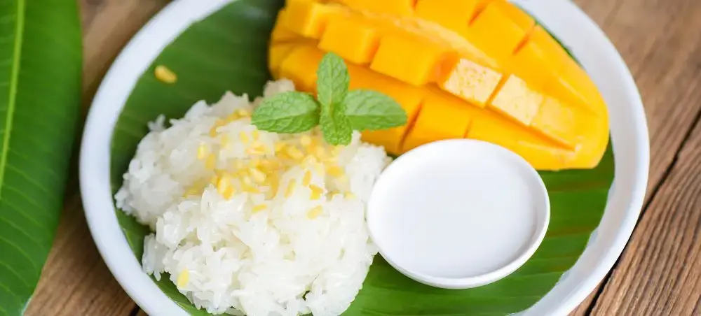 Traditional Thai mango sticky rice dessert with coconut milk served on banana leaf in white bowl