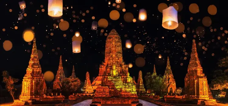 Ancient Buddhist temples illuminated at night with floating lanterns creating magical atmosphere in Thailand