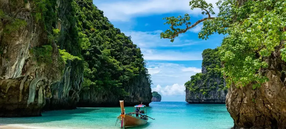 Traditional longtail boat anchored in turquoise lagoon surrounded by limestone cliffs in tropical Thailand