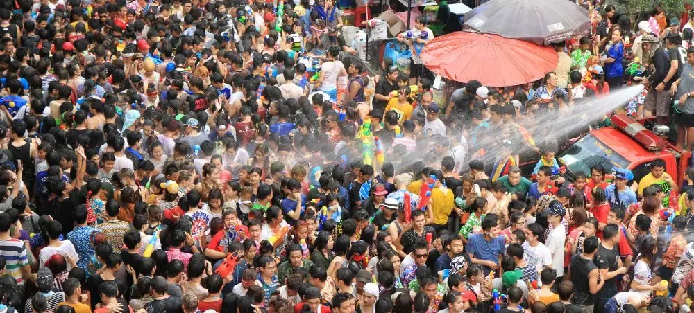 Massive crowd celebrating Songkran water festival in Thailand with colorful water guns and umbrellas