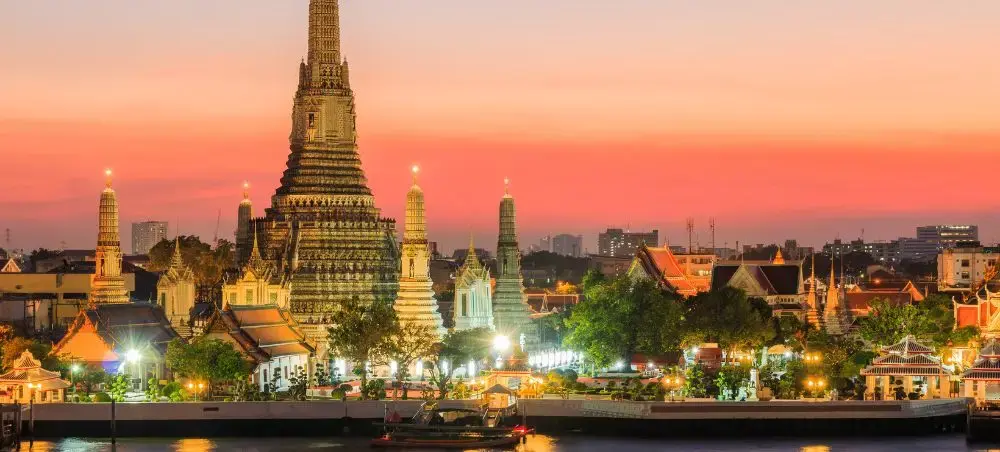 Wat Arun temple illuminated at sunset along Bangkok's Chao Phraya River showcasing Thailand's cultural heritage