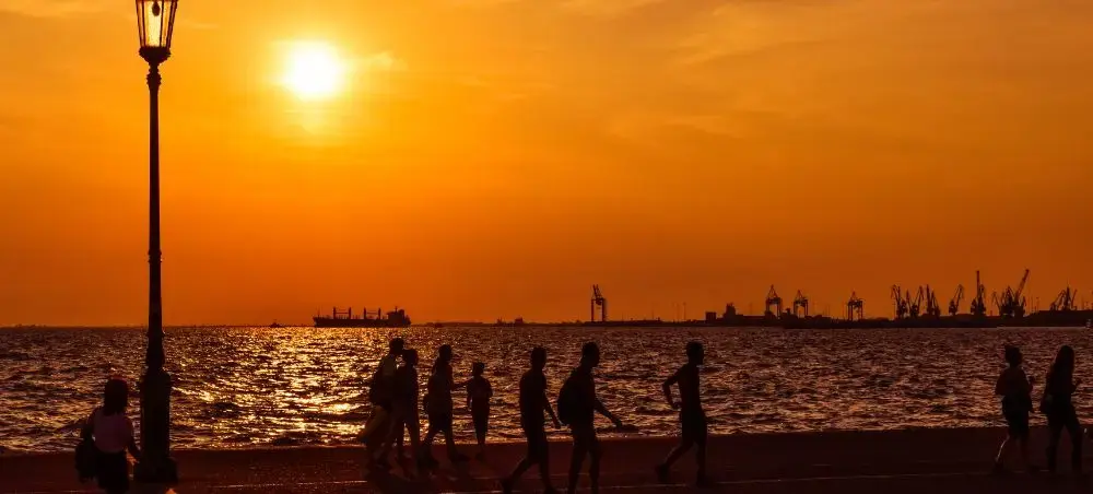Golden sunset over Thessaloniki waterfront with silhouettes of people strolling along the harbor promenade