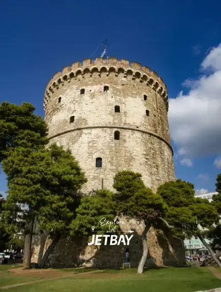 White Tower of Thessaloniki surrounded by lush green trees under blue Mediterranean sky in Greece