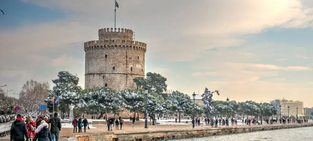 Historic White Tower of Thessaloniki waterfront with snow-covered trees and visitors exploring Greece's cultural landmark