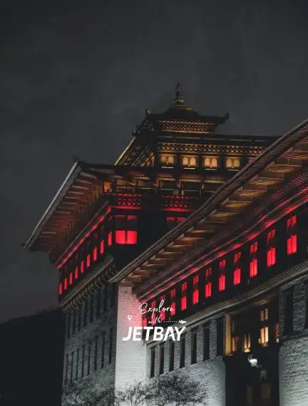 Traditional Bhutanese architecture illuminated at night in Thimphu with Jetbay branding overlay