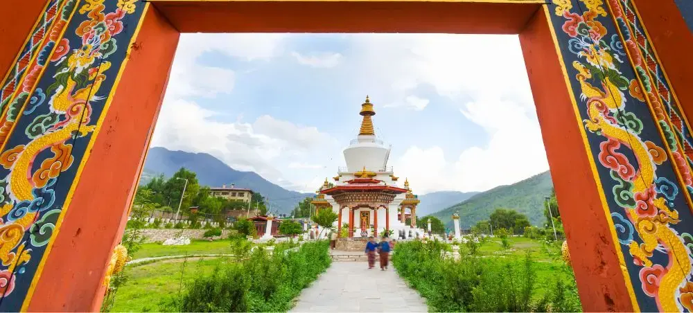 Traditional Bhutanese gateway frames white Buddhist stupa surrounded by mountains in Thimphu valley
