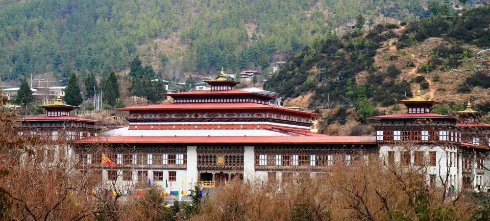 Traditional Bhutanese monastery complex with ornate architecture nestled in forested mountains of Thimphu