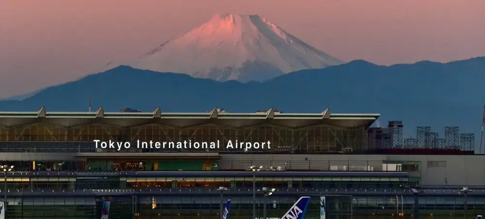 Tokyo International Airport terminal with Mount Fuji's snow-capped peak glowing pink at sunset