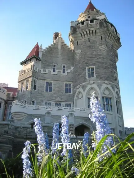 Historic Casa Loma castle with red turrets and stone architecture surrounded by purple flowers in Toronto