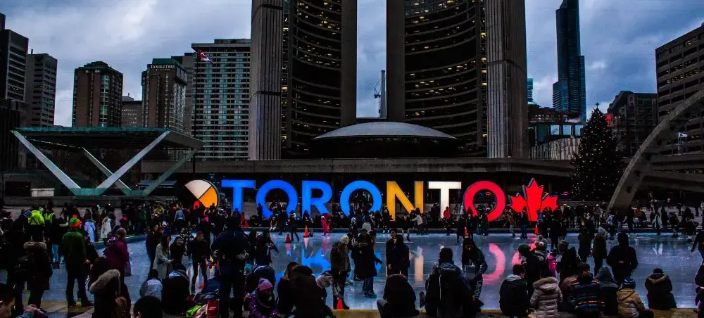 Toronto city hall plaza with illuminated TORONTO sign and ice skating rink surrounded by downtown skyscrapers