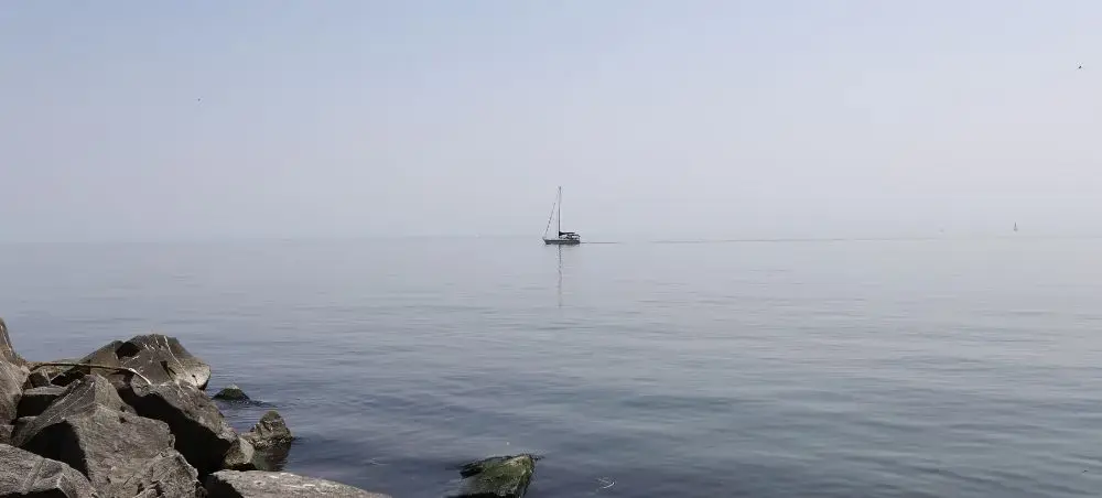 Serene sailboat anchored in calm waters near Toronto's rocky shoreline on a peaceful misty morning