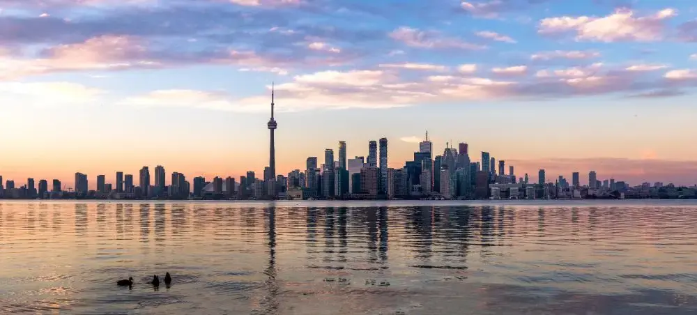 Toronto skyline at sunset with CN Tower and downtown skyscrapers reflecting in Lake Ontario waters