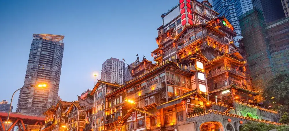 Traditional Chinese architecture illuminated at dusk contrasts with modern skyscrapers in vibrant cityscape