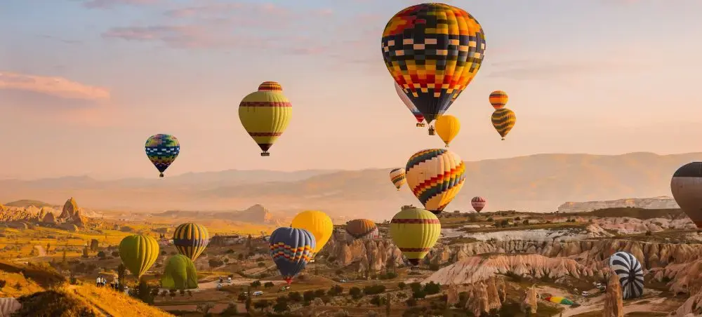 Colorful hot air balloons floating over Cappadocia's unique rock formations during golden hour sunrise