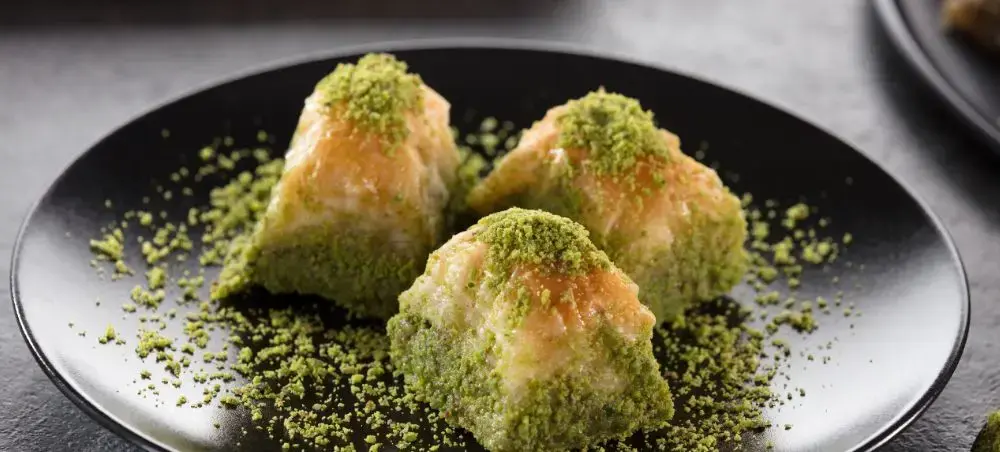 Traditional Turkish baklava dessert with pistachio coating served on elegant black plate for luxury dining
