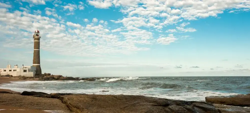 Historic lighthouse stands sentinel on Uruguay's dramatic coastline with rolling waves and expansive sky