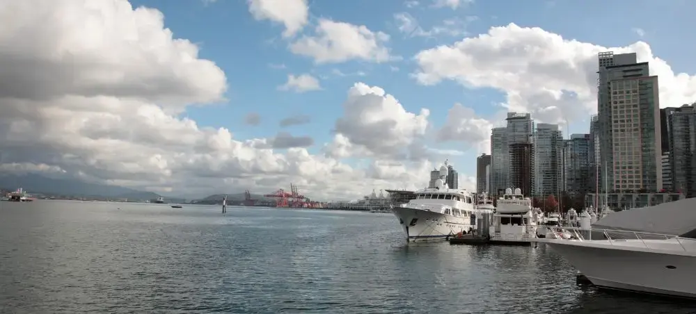 Luxury yachts docked at Vancouver's Coal Harbour marina with downtown skyline and mountains beyond