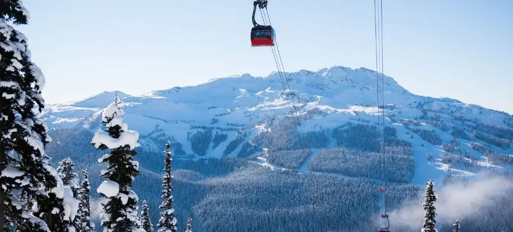 Red cable car gondola ascending over snow-covered mountain peaks and ski slopes in Vancouver's alpine region