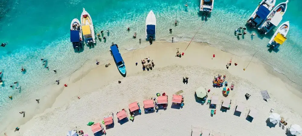 Aerial view of pristine Venezuelan beach with turquoise waters, white sand, colorful boats and beachgoers