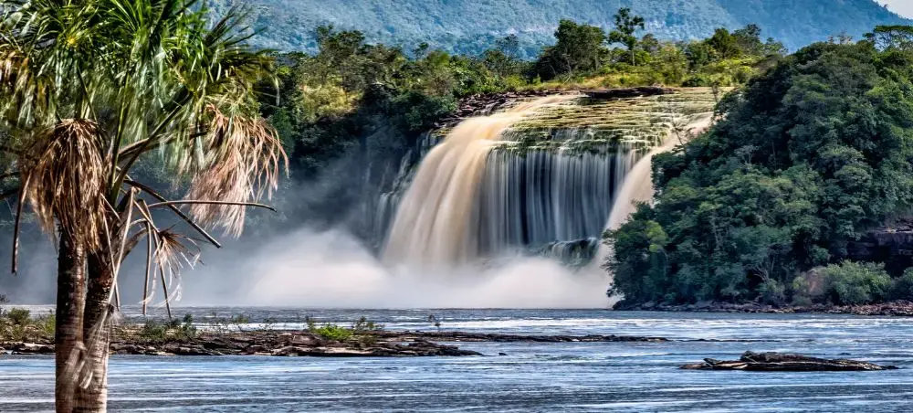 Spectacular Canaima Falls cascading through lush Venezuelan rainforest with palm trees and misty waters