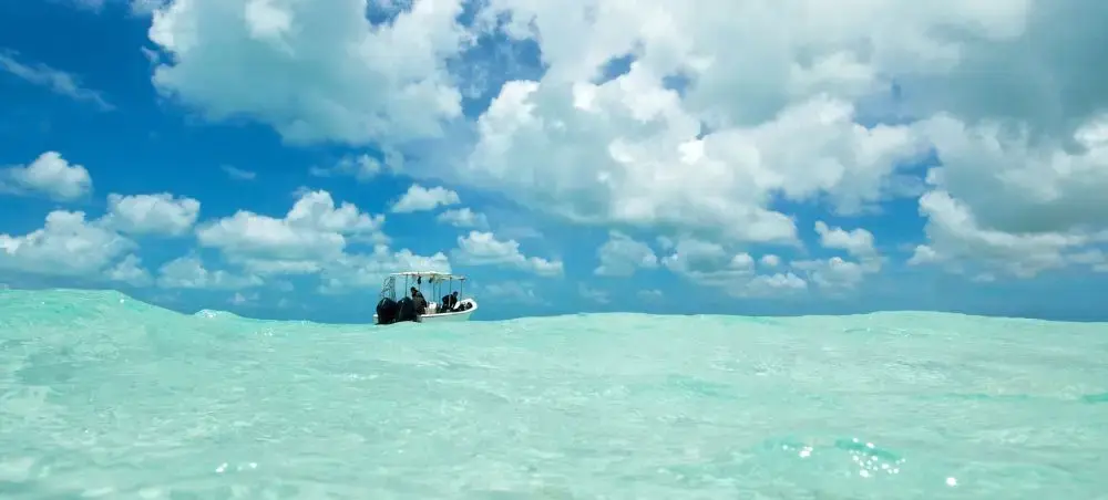 Small boat floating in crystal-clear turquoise waters under dramatic cloudy skies in Venezuela