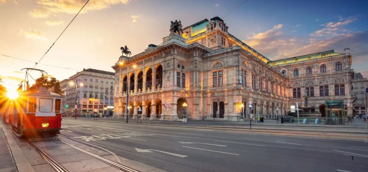 Vienna State Opera House illuminated at golden hour with traditional red tram passing by historic square