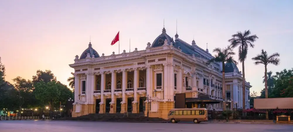 Hanoi Opera House illuminated at sunset with French colonial architecture and palm trees in Vietnam