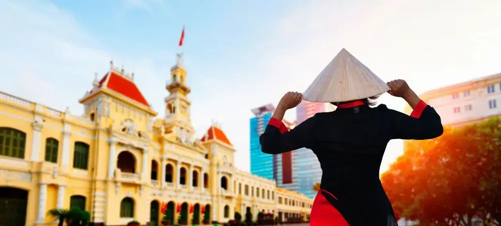 Traveler wearing traditional Vietnamese conical hat admiring historic colonial architecture in Ho Chi Minh City