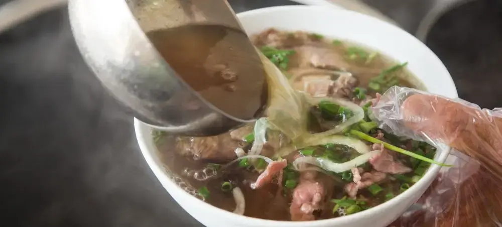 Traditional Vietnamese pho soup with beef and herbs being served, showcasing authentic cuisine culture