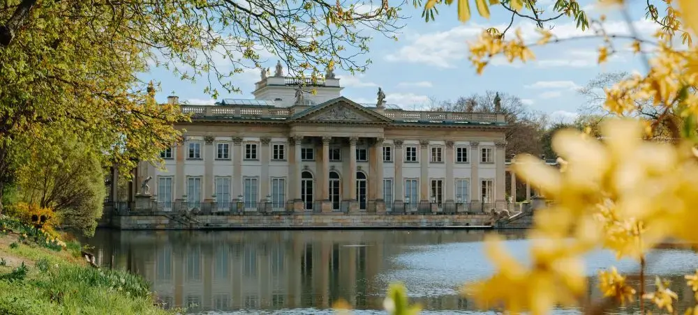 Elegant neoclassical palace reflected in tranquil waters surrounded by autumn foliage in Warsaw Poland