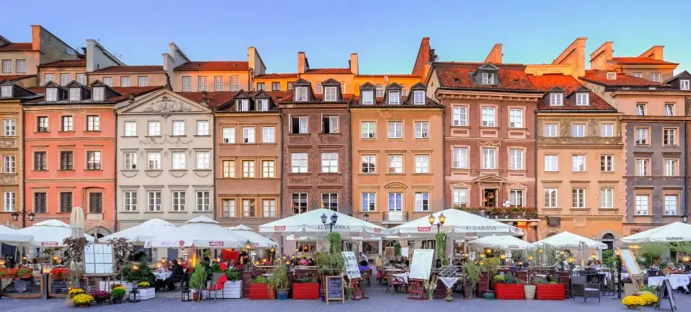 Historic colorful townhouses line Warsaw's Old Town Market Square with outdoor dining terraces at sunset