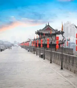 Ancient city wall fortifications in Xian with traditional Chinese watchtowers under dramatic sunset sky